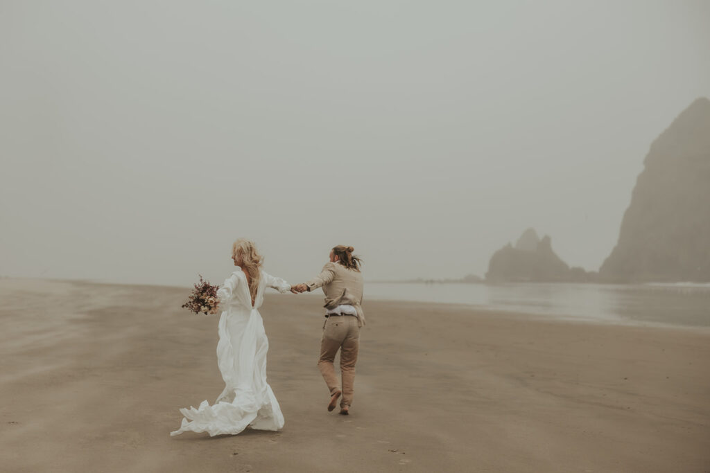 couple holding hands running around the beach 
